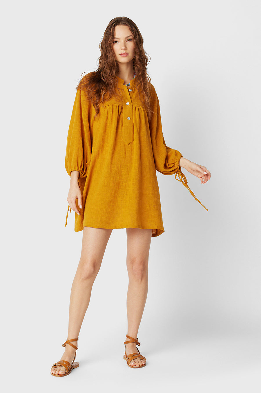 Brunette Model wearing the lady & the sailor Billow Sleeve Mini Dress on the beach in Golden Gauze.