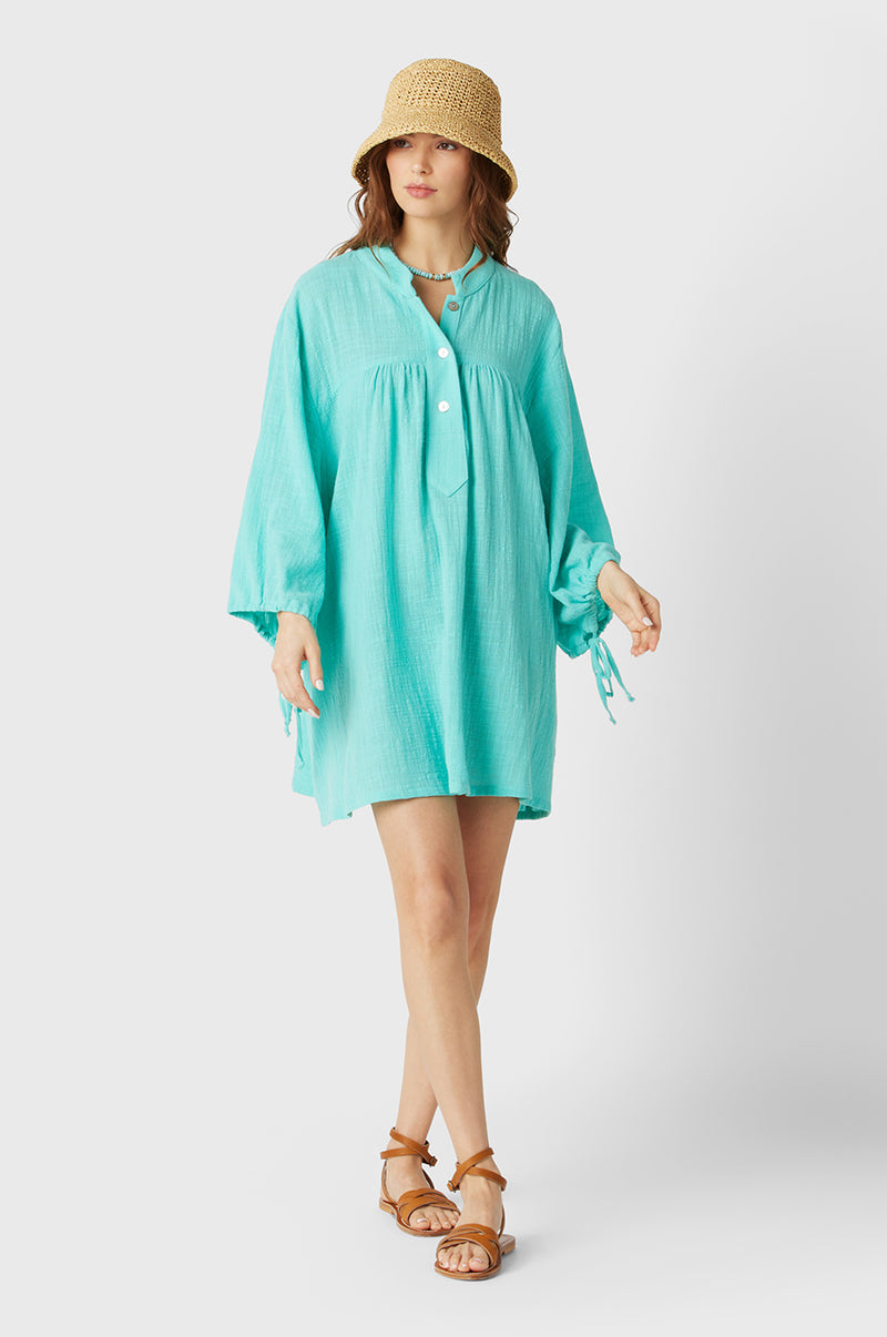 Brunette Model wearing the lady & the sailor Billow Sleeve Mini Dress on the beach in Aqua Gauze.