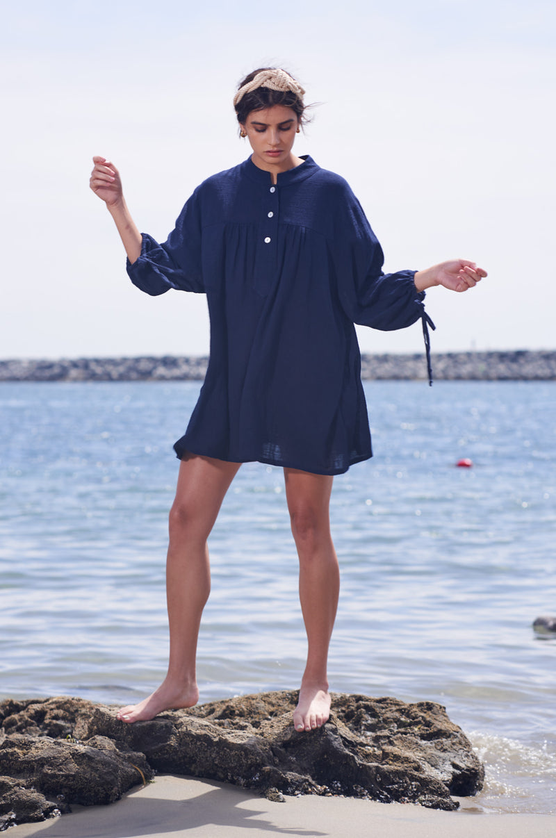 Brunette Model wearing the lady & the sailor Billow Sleeve Mini Dress on the beach in Navy Gauze.