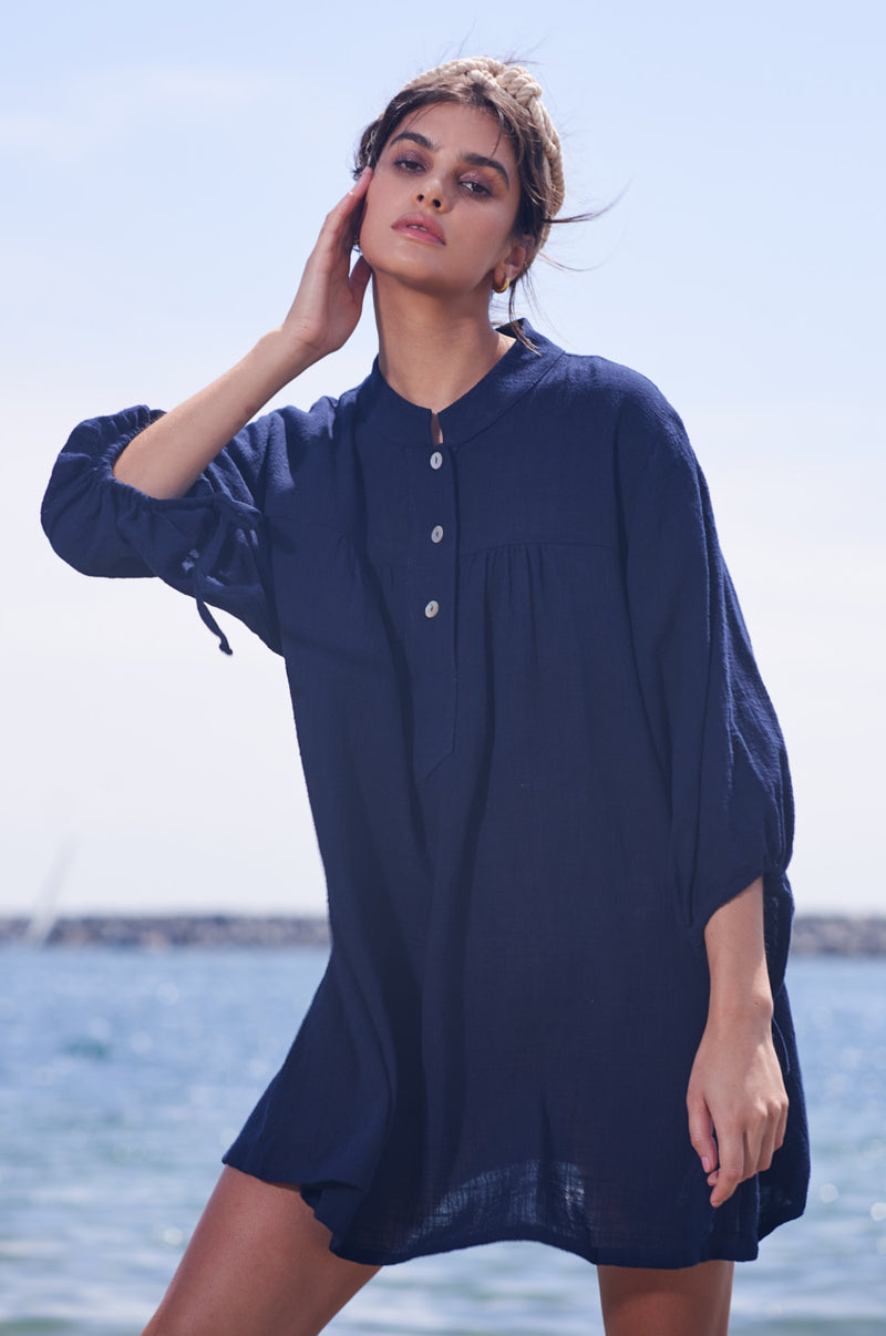 Brunette Model wearing the lady & the sailor Billow Sleeve Mini Dress on the beach in Navy Gauze.
