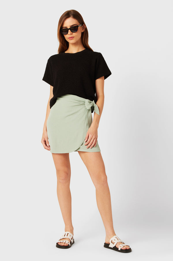 Brunette Model wearing the lady & the sailor Wrap Mini Skirt in Seaglass Air Flow.